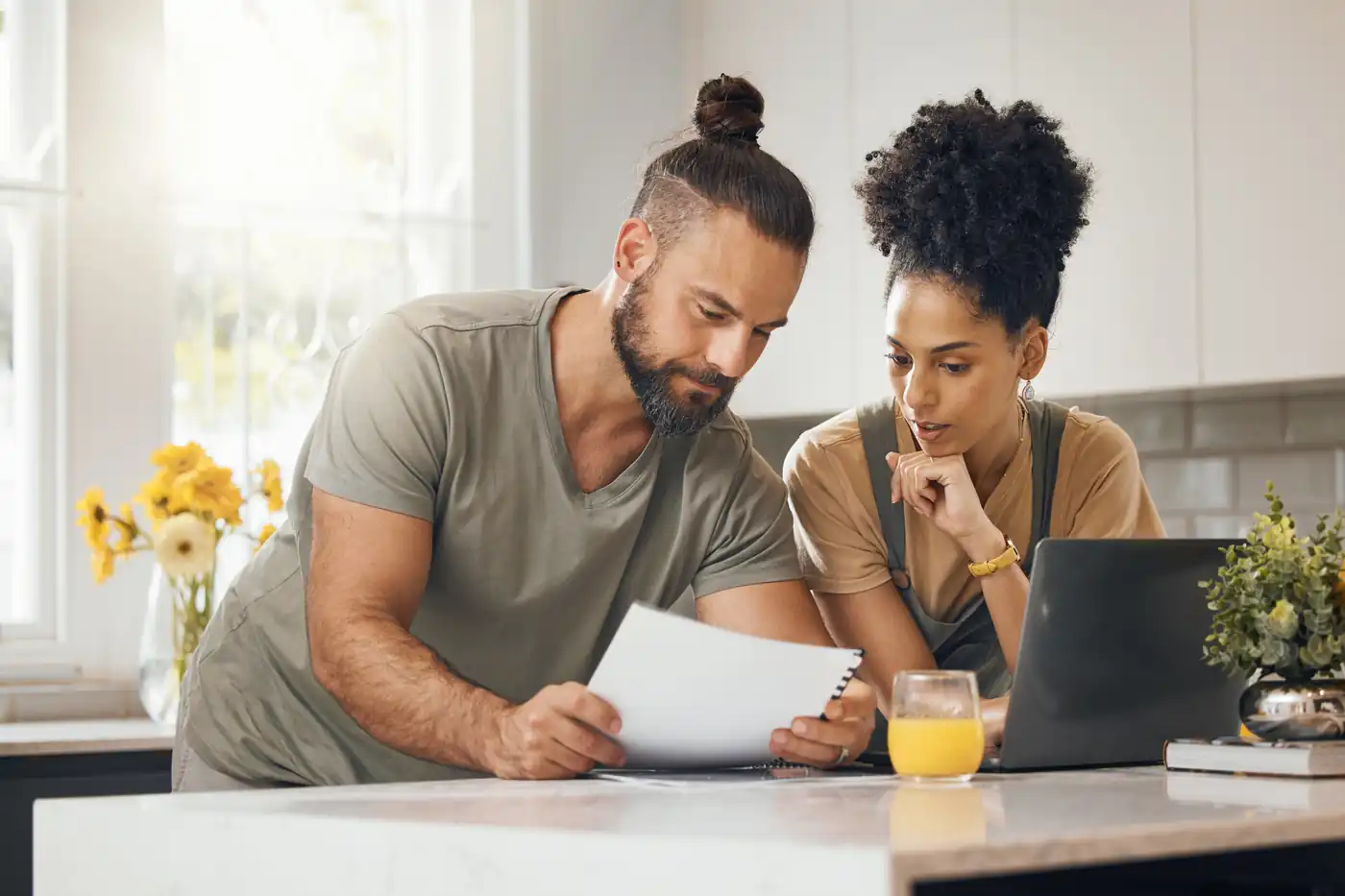 A man and a woman reading a letter together at the kitchen counter at home, a laptop beside them